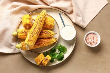 Lezzetli ızgara mısır koçanı ve kahverengi arka planda sos tabağı.