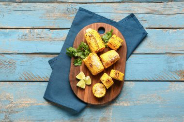 Lezzetli ızgara mısır koçanları ve mavi ahşap arka planda maydanozlu tahta.