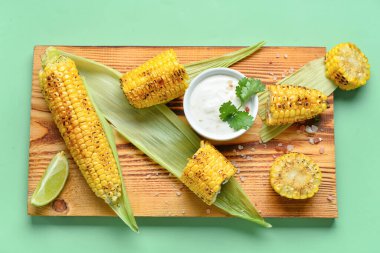 Lezzetli ızgara mısır ve yeşil arka planda sos koçanlarıyla ahşap tahta.