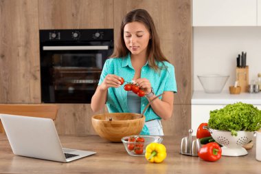 Genç kadın mutfakta domatesli sebze salatası hazırlıyor.