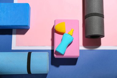 Güneş kremi şişesi, yoga minderleri ve renkli arka plan blokları olan kompozisyon