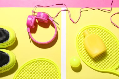 Renkli arka planda güneş kremi, kulaklık ve spor malzemesi içeren kompozisyon