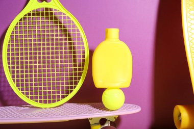 Güneş kremi, kaykay, tenis raketi ve renk arkaplanlı top içeren kompozisyon