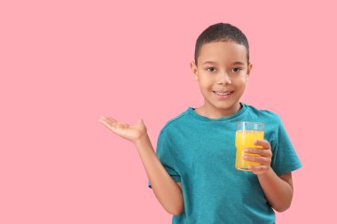 Bir bardak portakal suyu olan küçük Afro-Amerikalı çocuk pembe arka planda bir şey gösteriyor.