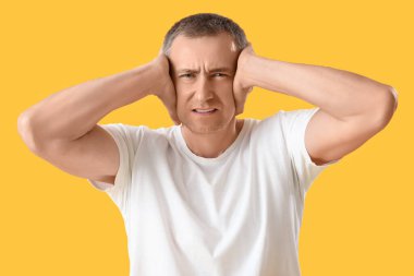 Turuncu arka planda gürültüden muzdarip stresli olgun bir adamın portresi.