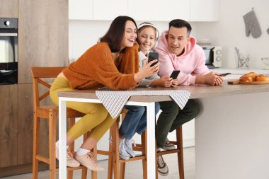 Cep telefonlu mutlu bir aile mutfaktaki masada dinleniyor.