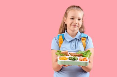 Sırt çantası ve pembe arka planda beslenme çantası olan mutlu küçük kız.