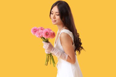 Sarı arka planda pembe yıldız çiçekleri olan güzel bir Asyalı gelin.