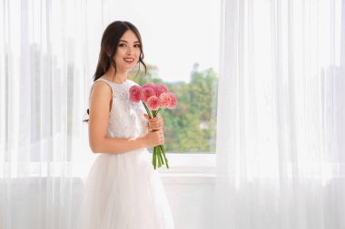 Evinin penceresinin yanında bir buket pembe yıldız çiçeğiyle güzel bir Asyalı gelin.