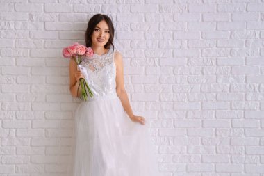 Beyaz tuğla duvarın yanında pembe yıldız çiçekleriyle güzel bir Asyalı gelin.