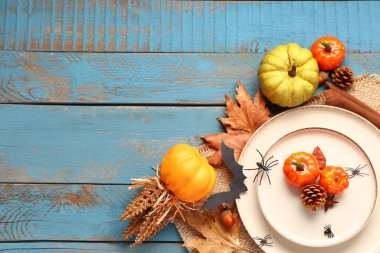 Cadılar Bayramı masası, balkabakları, sonbahar yaprakları ve mavi ahşap arka planda örümcekler.