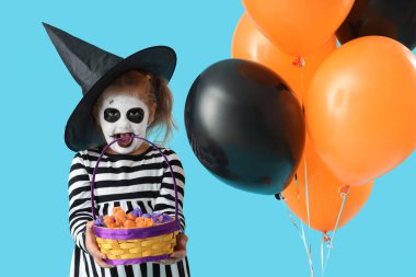 Cadılar Bayramı için giyinmiş küçük kız. Mavi arka planda balonlar ve şekerlerle.