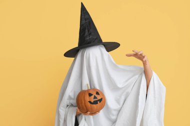 Cadılar bayramı kostümlü kadın hayalet ve cadı şapkası elinde balkabağı renginde arka planda