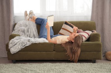 Evdeki kanepede uzanan defterli düşünceli kadın yazar.