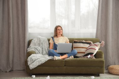 Kadın yazar evdeki kanepede dizüstü bilgisayar kullanıyor.