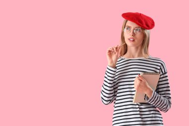 Pembe arka planda not defteri olan düşünceli bir kadın yazar.