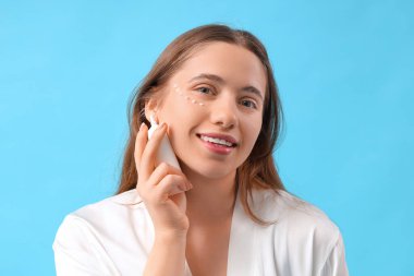 Mavi arka planda göz kremi olan genç bir kadın, yakın plan.