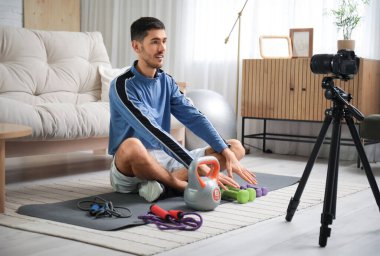 Atlama halatları, dambılları ve kettlebell kayıt videosu olan neşeli erkek blogcu.