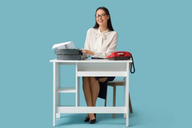 Mavi arka plandaki masada daktiloda yazan genç sekreter.