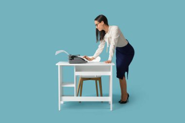 Masanın yanında mavi arka planda daktilosu olan güzel bir sekreter.