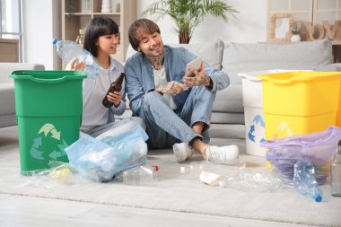 Çöp konteynırları olan genç bir çift evdeki tablet bilgisayardan bilgi topluyorlar. Geri dönüşüm kavramı