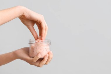 Gri arka planda doğal vücut ovma kavanozu olan kadın elleri, yakın plan