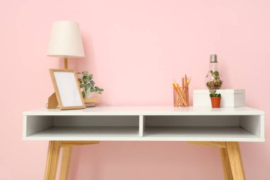 Lambalı şık bir iş yeri, boş fotoğraf çerçevesi ve pembe duvarın yanındaki kırtasiye malzemesi.