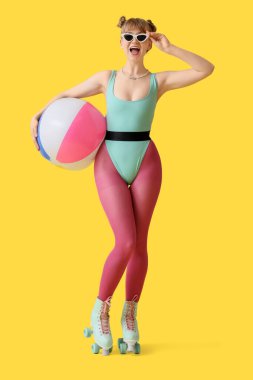 Sarı arka planda şişme topu olan patenli güzel, genç ve mutlu bir kadın.