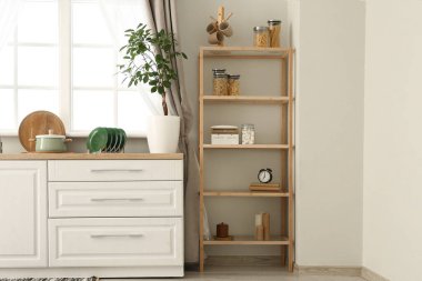 Beyaz tezgahlı, pencereli, ev bitkisi ve raf üniteli şık bir mutfak.