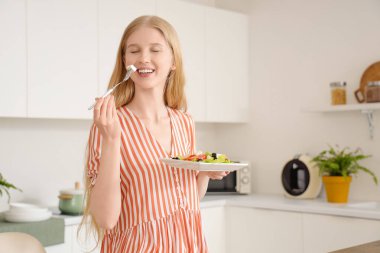 Mutfakta peynirli salata yiyen genç bir kadın.