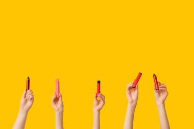 Sarı arka planda elektronik sigaraları tutan bir sürü el var.