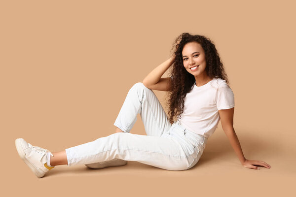 Счастливая молодая афроамериканка сидит на бежевом фоне