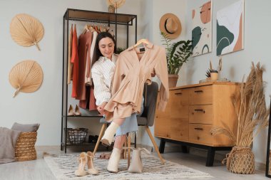 Şık elbiseli genç bir kadın elbise rafının yanında oturuyor.