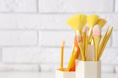 Beyaz tuğla arka planda makyaj fırçaları olan tutucu