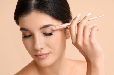 Bej arka planda makyaj fırçası olan güzel bir genç kadın.