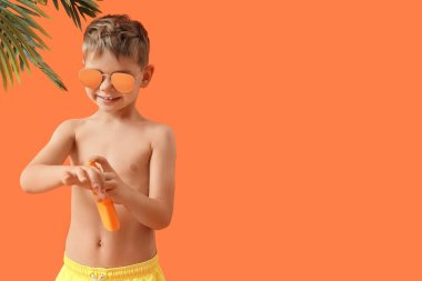 Güneş kremi süren ve portakal rengi arka planda palmiye yaprakları olan sevimli bir çocuk.