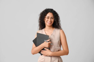 Gri arka plan üzerine not defterleri olan genç bir Afro-Amerikalı iş kadını.