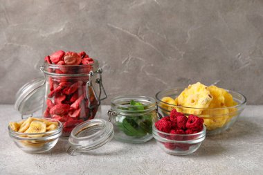 Glass bowls and jars of different dehydrated fruits and berries on grey background clipart