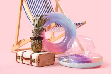 Şişirilebilir halkalar, güverte sandalyesi ve pembe arka planda ananas ve güneş gözlüğü olan bavul. Seyahat kavramı