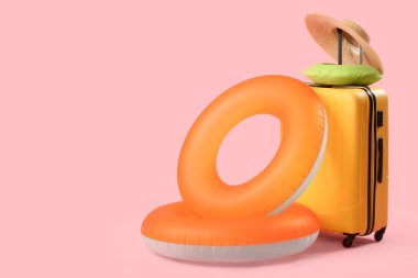 Şişme yüzük, pembe arka planda şapka ve boyun yastığı olan bavul. Seyahat kavramı