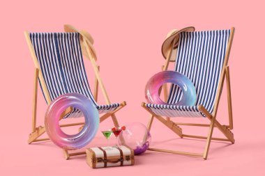 Şişirilebilir halkalar, güverte sandalyeleri ve pembe arka planda kokteyllerle dolu bavullar. Seyahat kavramı