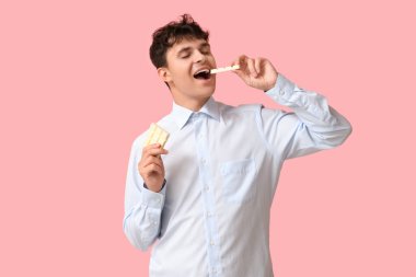 Yakışıklı genç adam pembe arka planda beyaz çikolata yiyor.