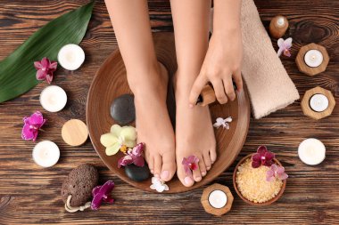 Kadın spa pedikür tedavisi görüyor ve ahşap arka planda kozmetik ürünler uyguluyor.