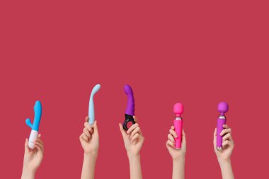 Kırmızı arka planda farklı vibratörlere sahip kadın elleri.