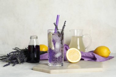 Bir bardak soğuk lavantalı limonata, çiçekler ve açık arkaplanda şurup.