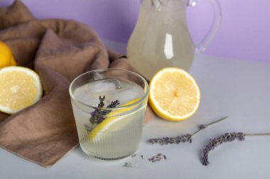 Bir bardak soğuk lavantalı limonata ve gri masada çiçekler.