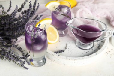 Açık arkaplanda soğuk lavantalı limonata, çiçek ve şurup bardakları.