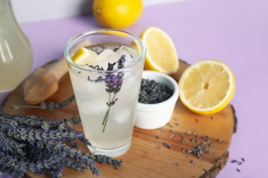Ahşap tahta tahta, bir bardak soğuk lavantalı limonata, limonlar ve renkli masa üzerinde çiçekler.