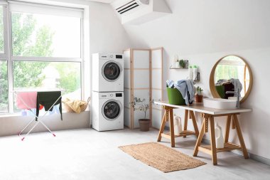 Çamaşır makinesi, kurutma makinesi, lavabo ve çamaşır sepetinin olduğu hafif banyonun içi.