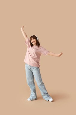 Kulaklıklı güzel bir kadın bej arka planda müzik dinliyor.